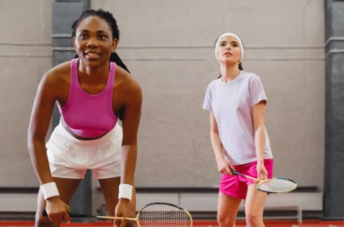 Two women playing badminton indoors, focusing on a competitive moment.