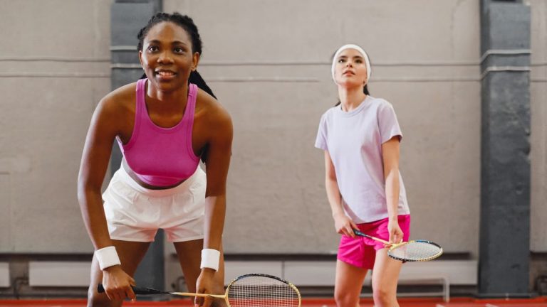 Two women playing badminton indoors, focusing on a competitive moment.